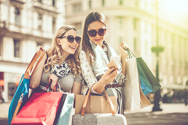 Summer shopping Cheerful beautiful women are shopping in the city. They are using smart phone, and one of them is holding a credit card. paris fashion stock pictures, royalty-free photos & images