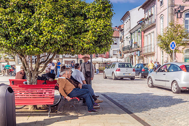 Ponte de Lima, Portugal - May 15, 2016: Cityscape of Ponte de Lima from the riverside, showing buildings and outdoor restaurants. Senior tourists and locals sitting on outdoor benches under a tree  and having a discussion.