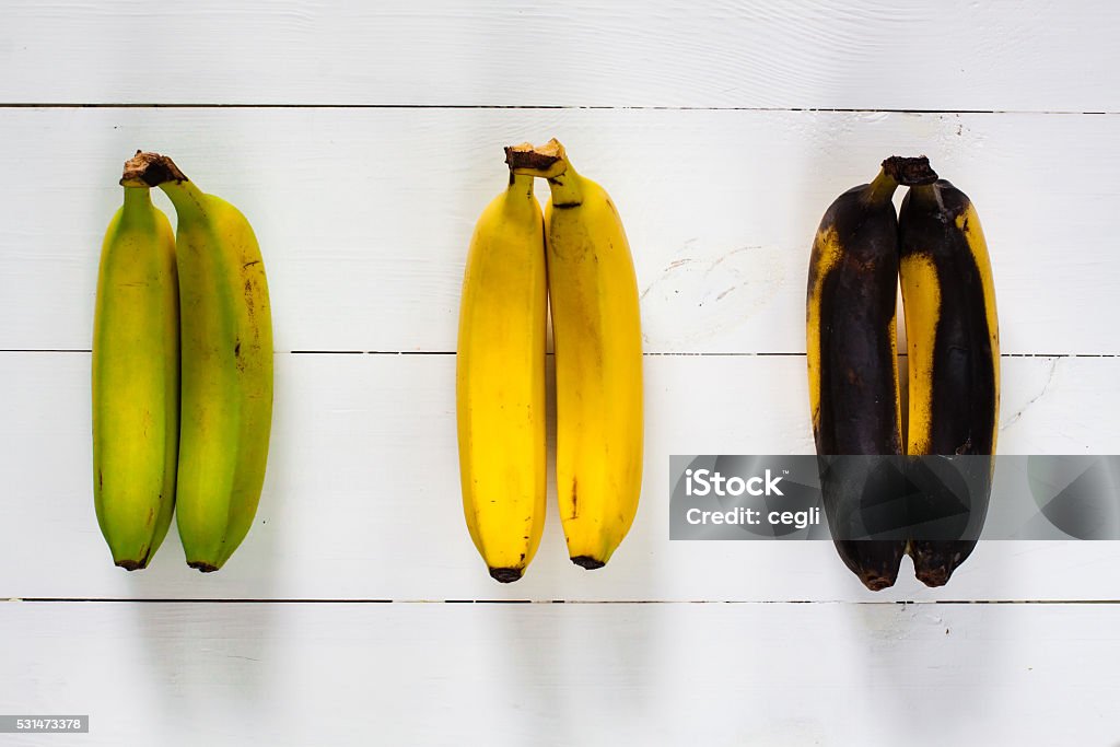 Green, yellow and black bananas. Green, yellow and black bananas arranged in a row on white wooden table. Banana Stock Photo
