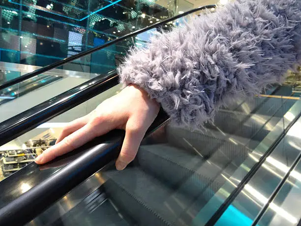 Photo showing a girl's hand on an escalator handrail / rail.  This is a concept image for germs, as research shows that the rail of escalators / moving stairs contains high levels of germs, including the cold and flu virus, and even blood, mucus, E. coli, feces and urine.  Therefore, many shoppers visiting department stores and shopping malls containing escalators avoid touching the handrail or use a hand sanitiser straight afterwards.
