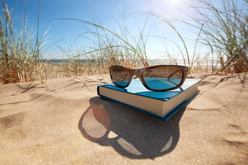Book and sunglasses on the beach for summer reading and relaxing