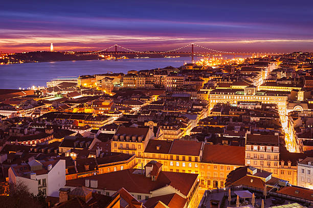 Night view over the Baixa and Chiado districts of Lisbon, Portugal, with the 25 de Abril Bridge over the Tagus river in the background.