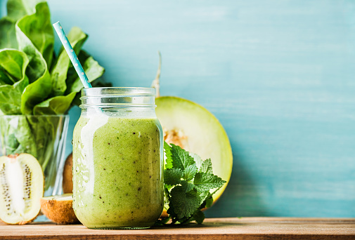 Freshly blended green fruit smoothie in glass jar with straw. Turquoise blue background, copy space