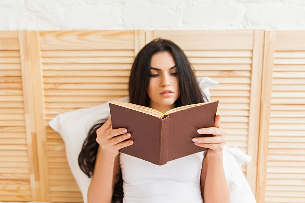 istock Woman sitting in bed while reading a book 531479710