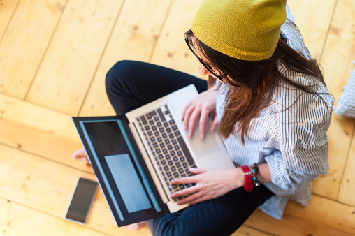 Hipster woman sitting on the floor using a laptop and mobile phone