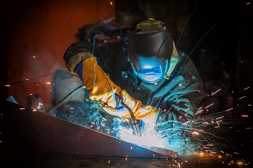 Close-up view of thin steel sheets welding. Selective focus. People working in engineering industrial production.