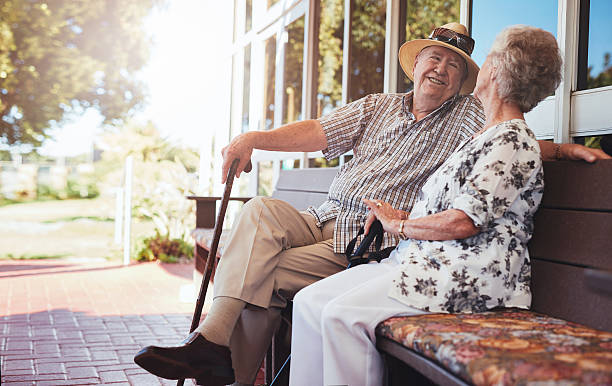 Happy senior couple relaxing on bench outside their house Loving senior couple having a chat while sitting on a bench outside their home. Happy senior couple relaxing on bench together. cottage life stock pictures, royalty-free photos & images