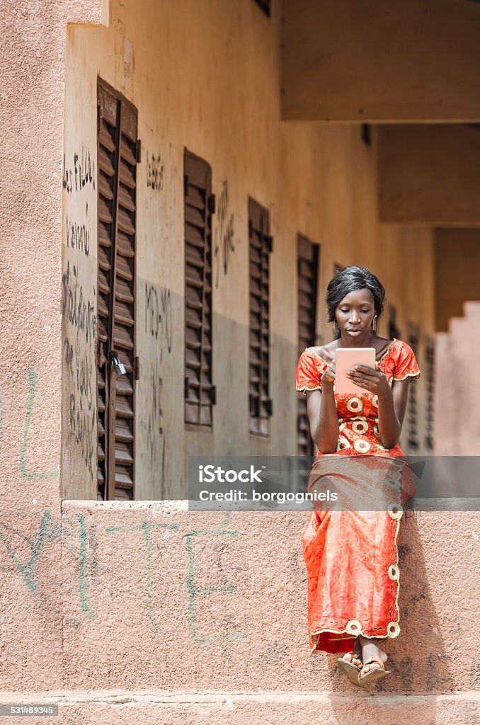 Technology Symbol: African College Girl Learning Lesson on Tablet Computer Street Shot of an African Ethnicity young woman working on business holding her technology item in a university in Bamako, Mali. University classroom class school environment. Africa Stock Photo