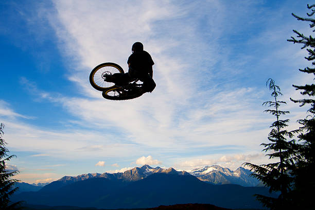 A male mountain bike rider hits a jump at sunset.
