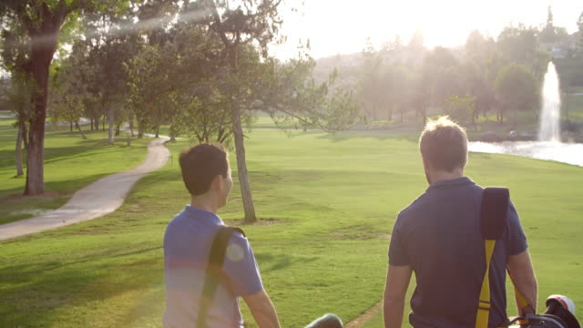 Slow Motion Shot Of Male Golfers Walking Along Fairway