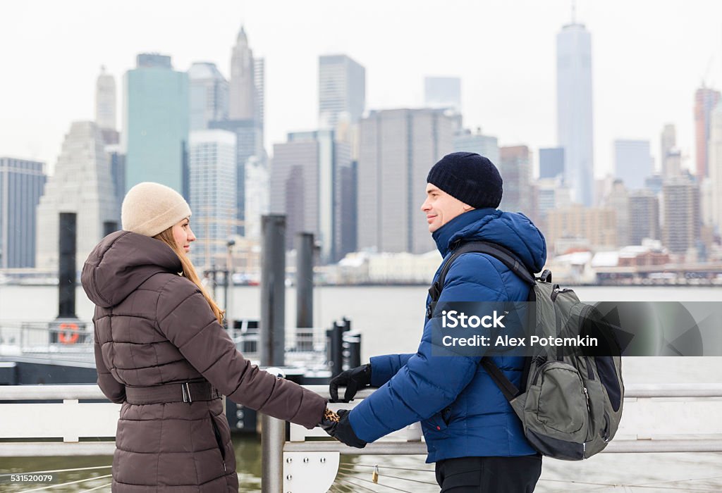 Young couple, man and woman, in the Manhattan Young tourists, couple, man and woman, in the Brooklyn Bridge Park in front of Manhattan Downtown, on vacations. 2015 Stock Photo