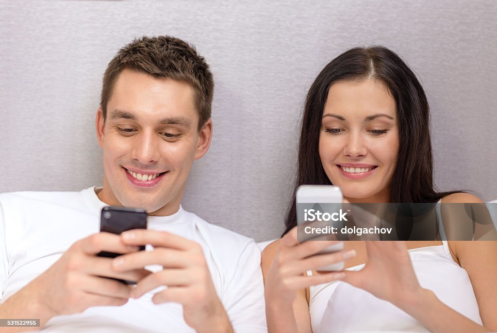 smiling couple in bed with smartphones hotel, travel, relationships, technology, intermet and happiness concept - smiling couple in bed with smartphones 2015 Stock Photo