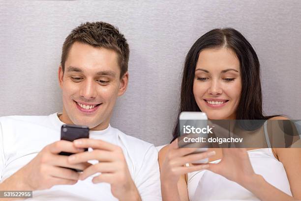 Smiling Couple In Bed With Smartphones Stock Photo - Download Image Now - 2015, Addiction, Adult