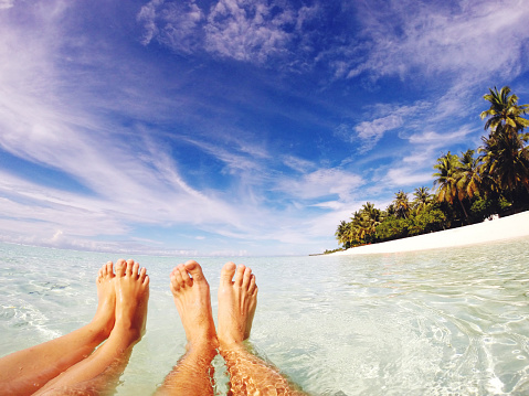 Happy feet in tropical paradise, relaxing in a water by the seaside; first person point of view