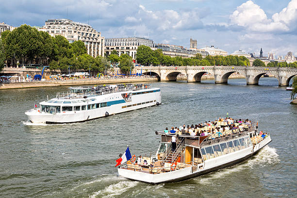 full of tourists sightseeing boats on Seine River near Ile de la Cite, a famous Pont Neuf  is seen in the background, Paris, France