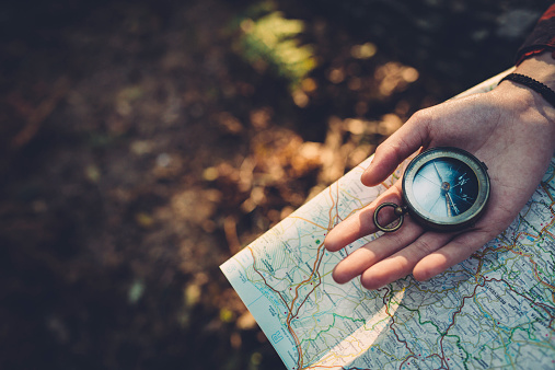 A tranquil forest and peaceful lake set the stage as a woman's hand holds a compass symbolizing guidance and the adventurous spirit of exploration in the great outdoors.