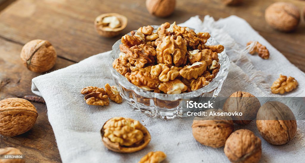 Glass bowl with walnuts on rustic homespun napkin. Healthy snack. Glass bowl with walnuts on rustic homespun napkin. Healthy snack on old wooden background. Walnut Stock Photo
