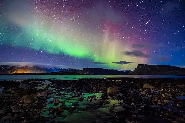 A typical Nordic nightscape and very famous location for travelers and adventurers from all over the world - Iceland with the spectacular celestial lights Aurora Borealis above into the winter night sky and amazing partly reflected Northern lights and Moonset into the sea bed at low tide, which makes this Polar country popular spot for tourists willing to witness one of the greatest natural phenomenoms. Shot with Canon EOS 60D, wide 11mm angle lens, f2.8, ISO 3200, long exposure of 30 seconds.
