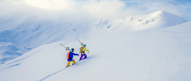 Two skiers preparing for an off-piste ride, walking up a snowy hill.