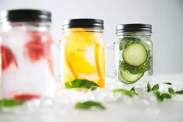 Close focus on last jar Healthy fresh cool homemade lemonades with sparkling water strawberry, cucumber,mint and orange isolated in smashed ice cubes on wooden table