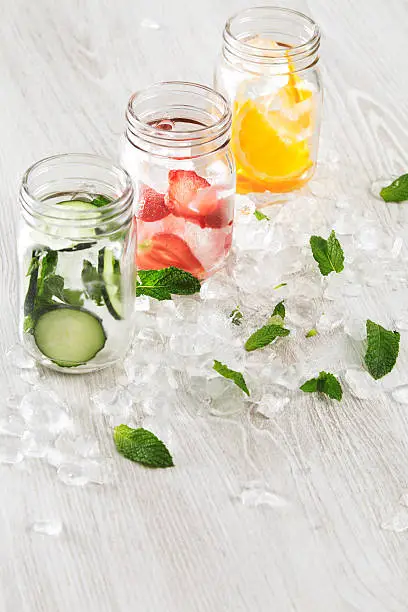 top view row rustic jars in crashed ice cubes with orange,strawberry,cucumber and mint prepared to make fresh homemade lemonade with sparkling water Cool down beverage in summer