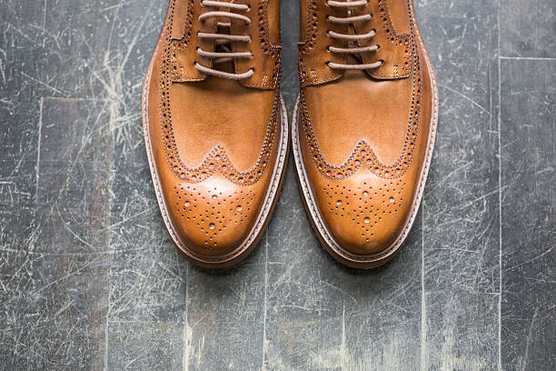 Tan Italian leather  designer brogues Horizontal top view of a pair of tan coloured designer Italian brogues. Against a dark wooden floor background. Space for copy, cropped. brogue photos stock pictures, royalty-free photos & images