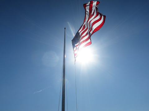 United States Flag at half mast (or rising) back-lit by the sun on a bright sunny day with blue sky. At Ft Sumter.