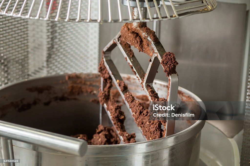 Brown dough inside industrial mixer. Brown dough inside industrial mixer. Dough pieces on mixer blade. Equipment at confectionery plant. High-quality cocoa flour. Dough Stock Photo