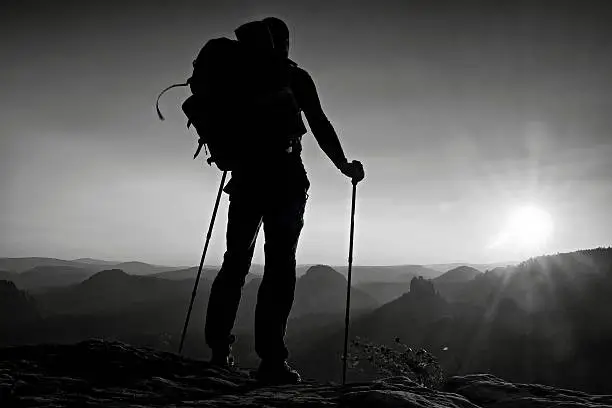 Photo of Tall backpacker with poles in hand. Sunny day in mountains