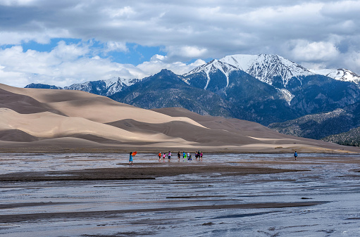 Mosca, Colorado, USA - May 06, 2016: A group kids are playing in Medano Creek at the base of sand dunes and snow-capped peaks of Sangre de Cristo Mountains as spring clouds passing over.