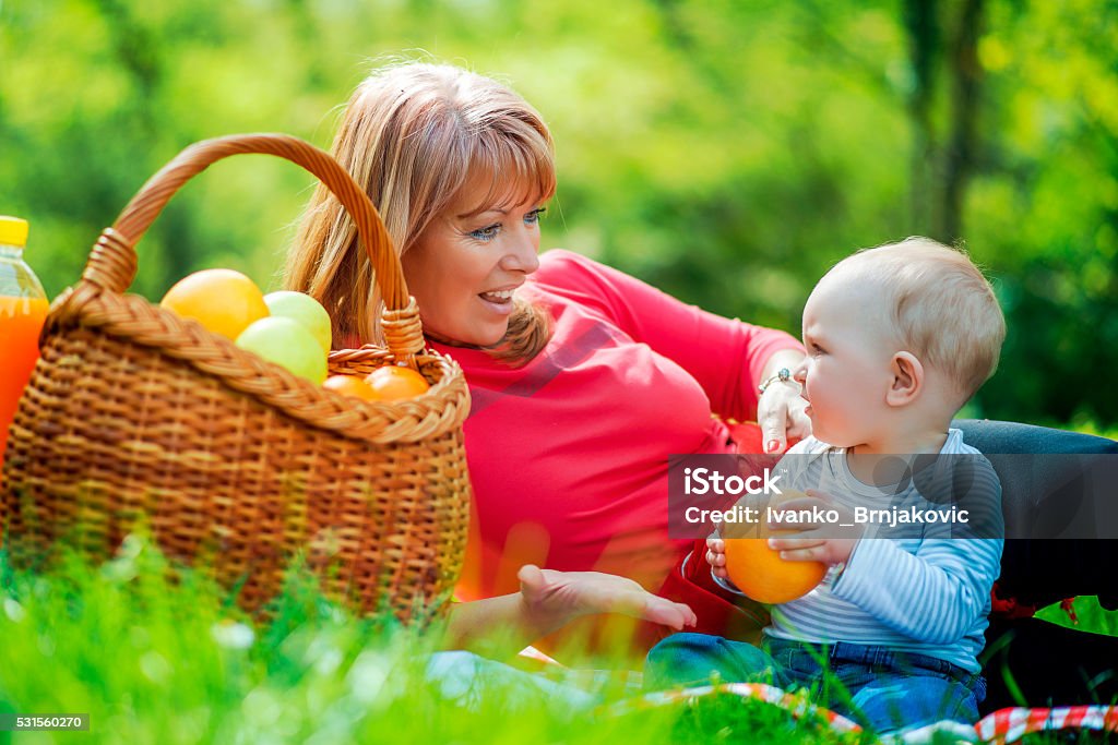 Playful mother having fun with her baby in nature Playful mother having fun with her baby in nature.Beautiful middle aged woman and her adorable little son having a picnic in sunny park. Embracing Stock Photo