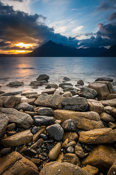 Wild beach ocean sunset over Cuillin mountains Highlands Skye Scotland Last rays of sunlight illuminating the wild rocky shore of Elgol Beach on the Isle of Skye beneath the dramatic rocky pinnacles of the Black Cuillin mountains deep in the Highlands of Scotland, UK. ProPhoto RGB profile for maximum color fidelity and gamut. elgol beach stock pictures, royalty-free photos & images