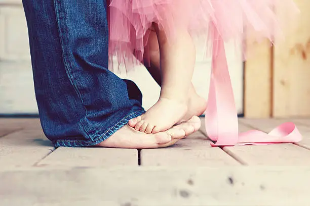 A baby girl in a pink tutu is dancing with her daddy. Cropped image of feet only. Copy space.