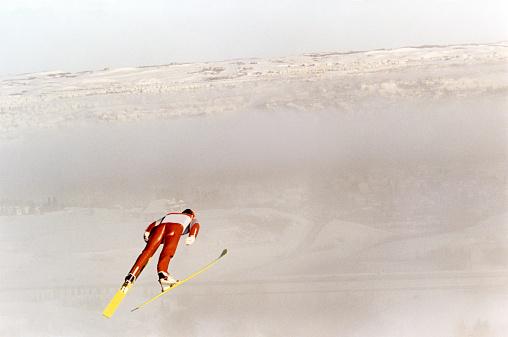 A male ski jumper takes flight on a foggy day.