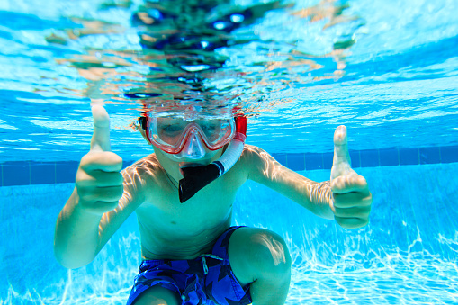 cute happy little boy swimming underwater with thumbs up