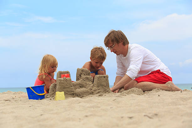 istock father with son and daughter building castle on beach 531608052