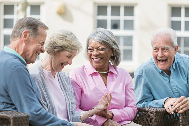 Multiracial senior friends sitting outdoors on patio talking A group of four multi-ethnic seniors sitting together on patio furniture outdoors, talking and laughing. They are in retirement, relaxed and enjoying spending time with friends. happiness four people cheerful senior adult stock pictures, royalty-free photos & images