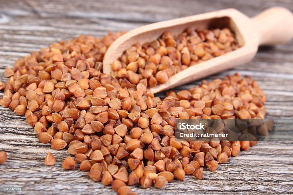 Destaque de groats de trigo sarraceno com uma colher de madeira com superfície - Foto de stock de Alimentação Saudável royalty-free