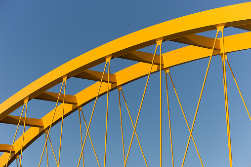 Fragment of a yellow bridge showing beams and cables against a steel blue sky shot in Utrecht, Netherlands