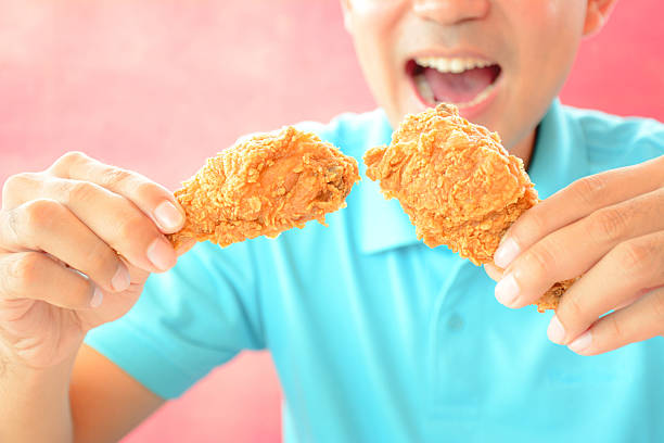 giovane uomo con pollo fritto gambe, su dove mangiare - deep fried people fried chicken foto e immagini stock