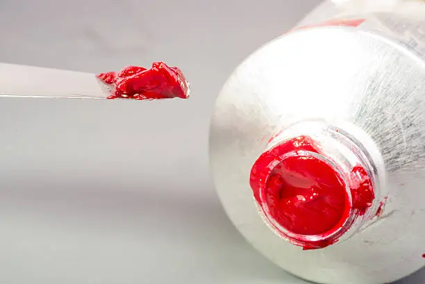 A small amount of red oil paint is taken with the tip of a paint knife from the tube of the paint.