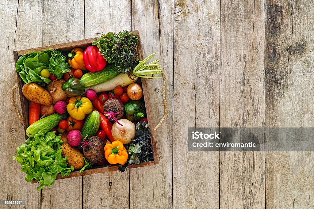 Old wooden crate packed full with fresh market salad vegetables. Various types of market fresh sald vegetables packed in an old wooden crate on an old wooden table. Salad vegetables includ types of lettuce, onion, tomato, cucumber, various colour capsicum, potato, radish, beetroot, Vegetable Stock Photo