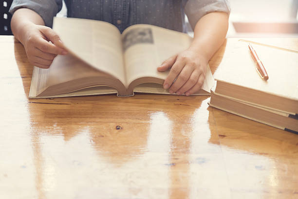 istock woman's hand reading book on wooden table 531629088