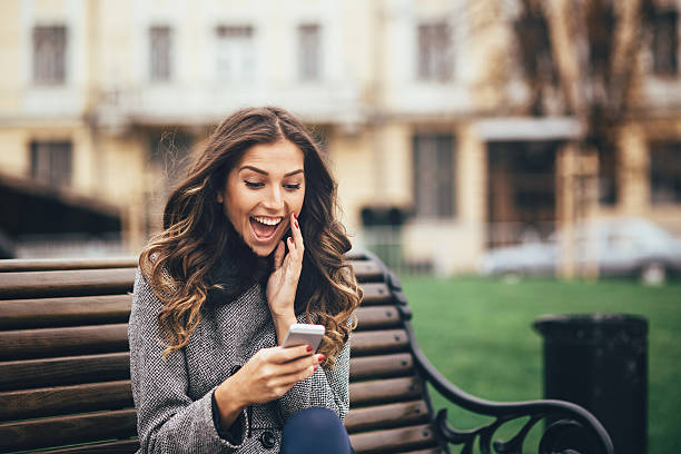 若い女性のスマート電話を屋外でリラクゼーション - よい知らせ ストックフォトと画像