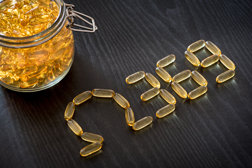 Omega 3-6-9 fish oil yellow softgels drawing omega 3-6-9  letters on wooden black table. Glass airtight jar.