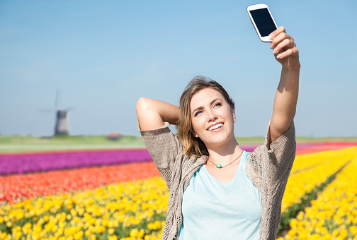 Woman taking selfie with blooming tulip field in Netherlands.
