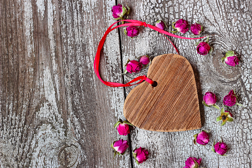 Wooden heart with red ribbon and small dried rosebuds on a wooden table
