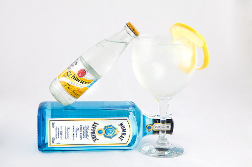 Valencia, Spain- october 31, 2013: Bombay Sapphire gin bottle, sweeps bottle and one glass of gin and tonic with ice and lemon, all isolated