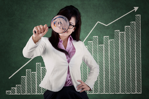 Successful entrepreneur holding magnifier to monitor business growth in front of business chart