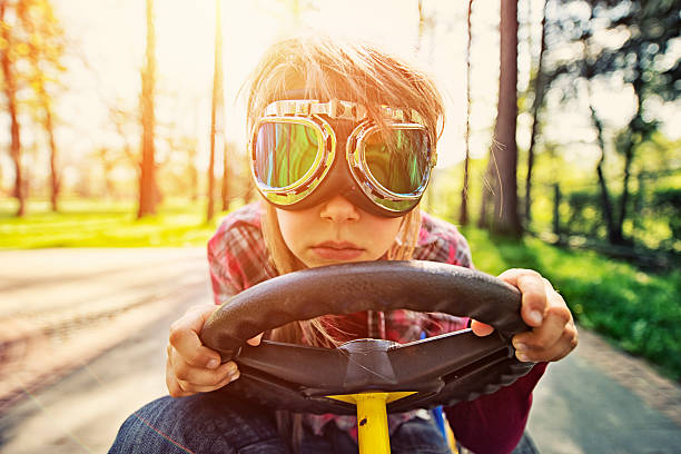 Little girl racing Little girl racing in a gokart. The girl is very serious despite looking very funny in large old fashioned racing goggles. Wide angle shot showing a surrounding forest in background as well as backlighting sunlight. kid toy car stock pictures, royalty-free photos & images